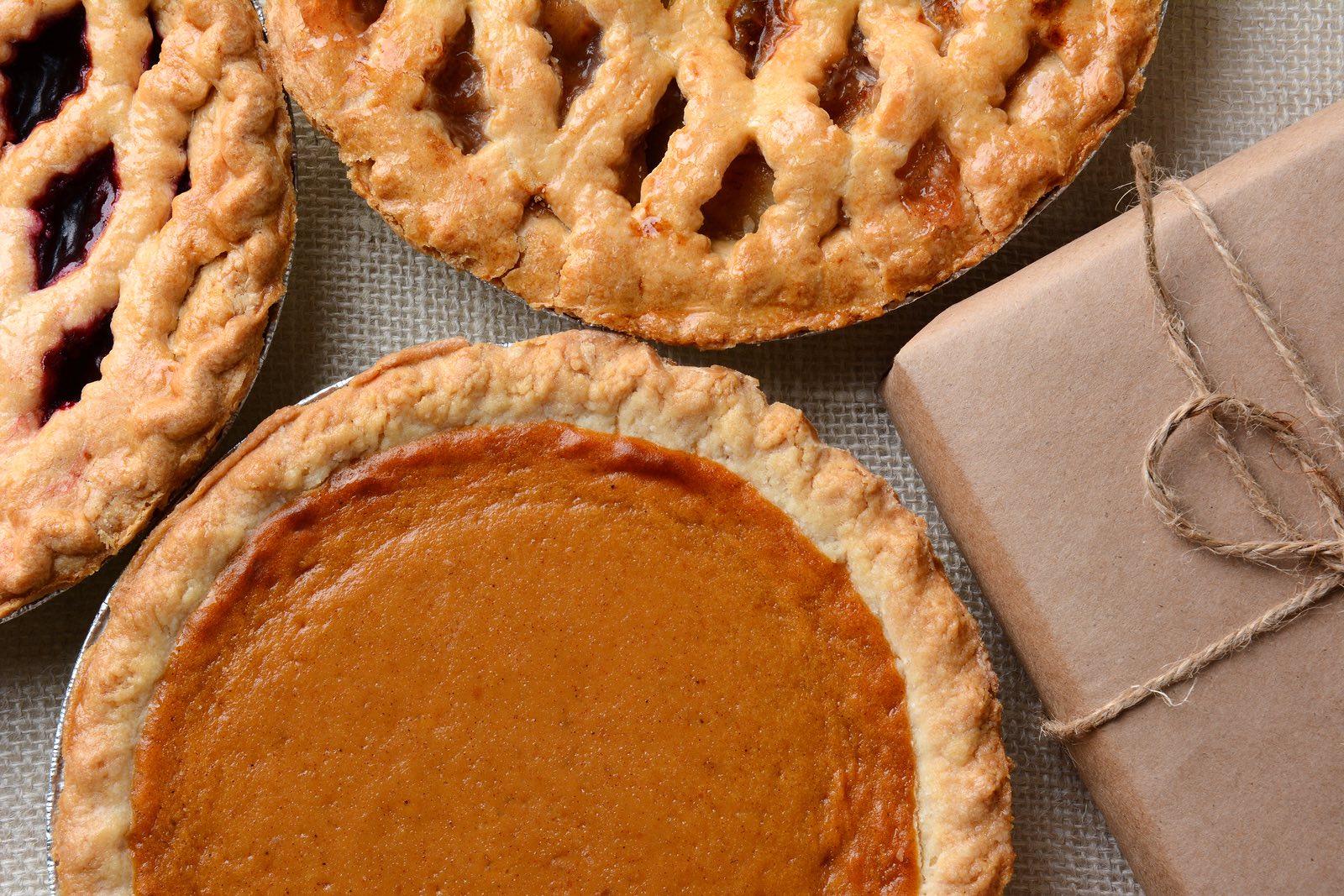 High angle closeup of three fresh baked holiday pies and a plain paper wrapped package. The traditio