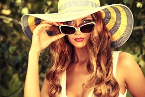 Beautiful young woman in elegant hat and sunglasses posing outdoor.