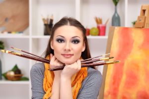 beautiful young woman painter at work, on room interior background